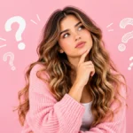Mujer con expresión de curiosidad y signos de interrogación sobre un fondo rosa, representando la pregunta qué es el Glow Up.